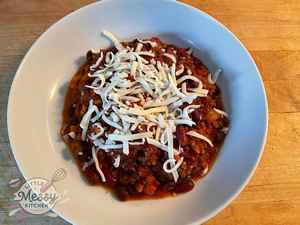 Serving of chili topped with shredded cheese in a white bowl.
