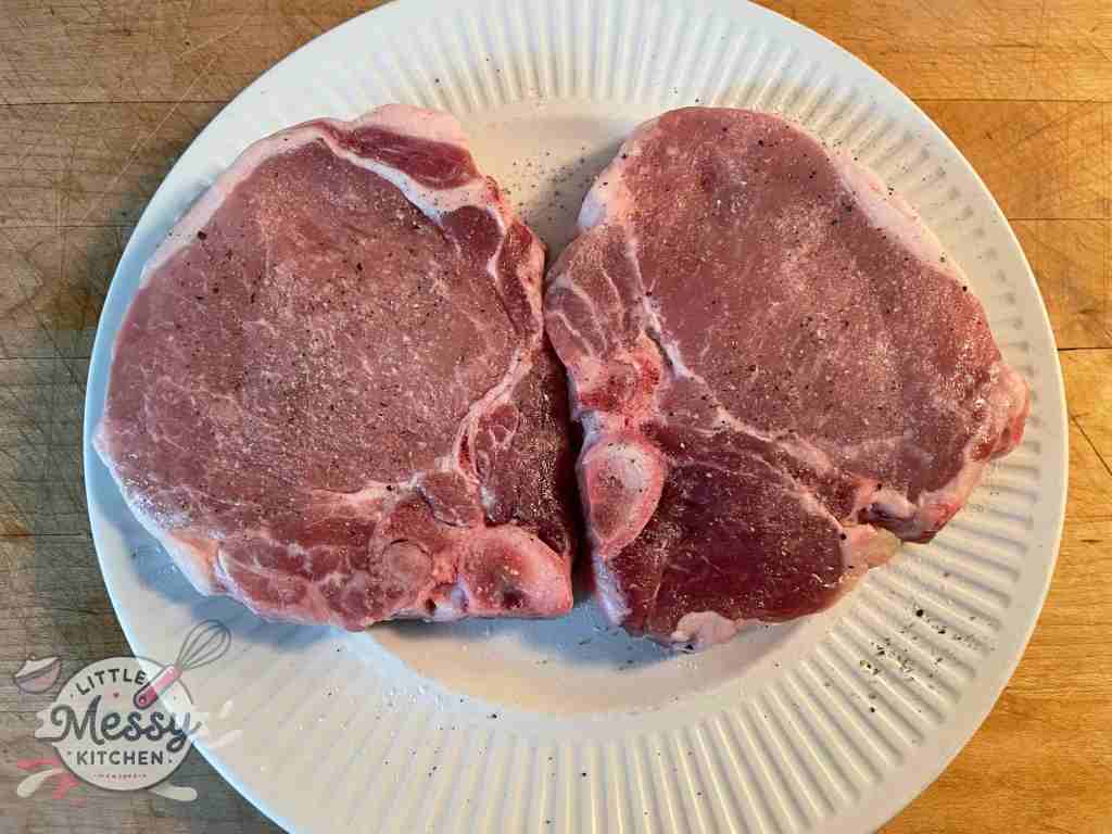 Uncooked pork chops seasoned with salt and pepper in plate.
