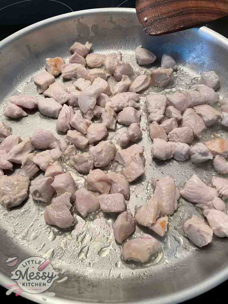 Diced chicken cooking in frying pan.