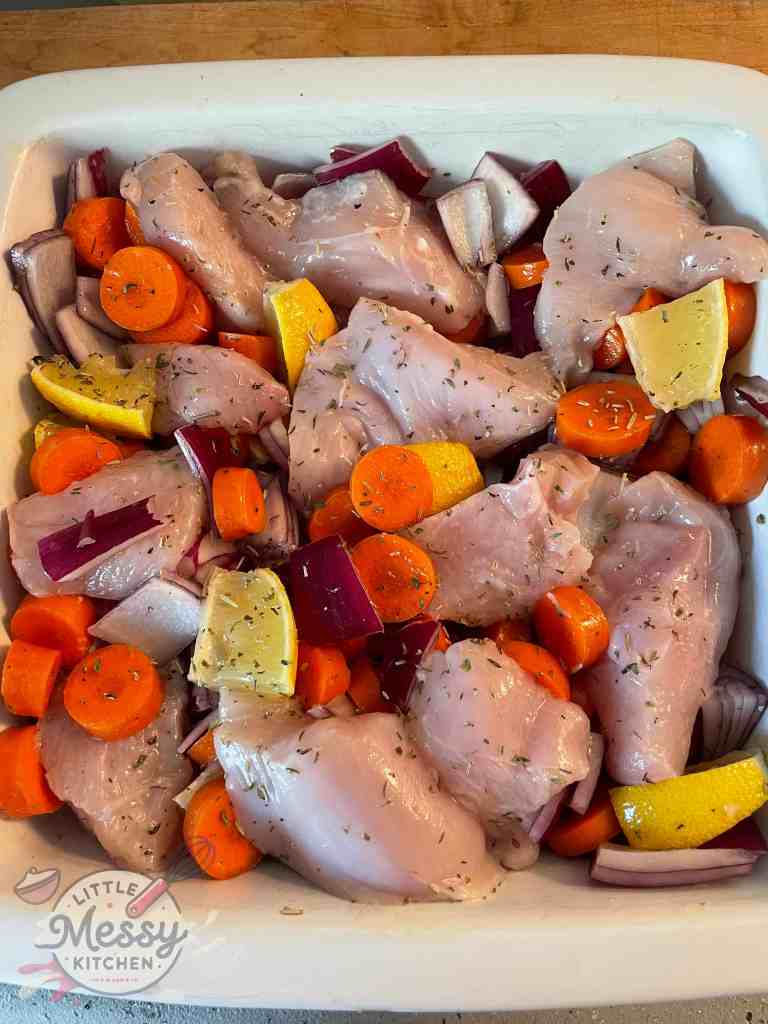Chicken breast, chopped carrots, red onion wedges, lemon and spices mixed in a baking dish.
