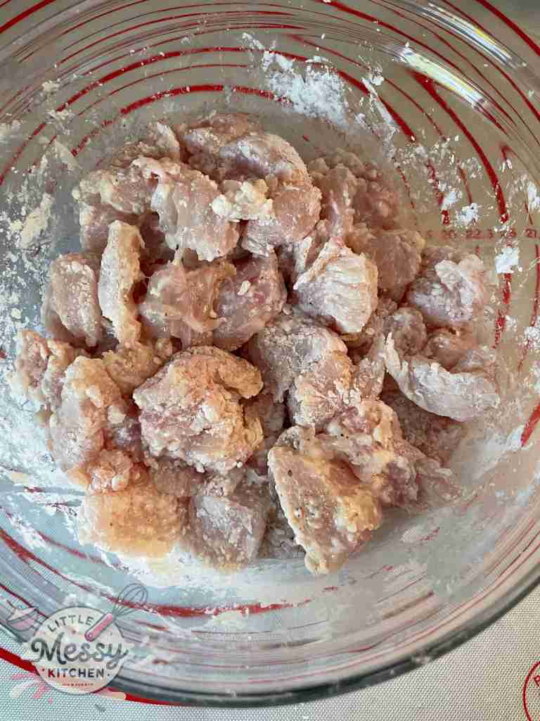 Chicken pieces coated in cornstarch in a mixing bowl.