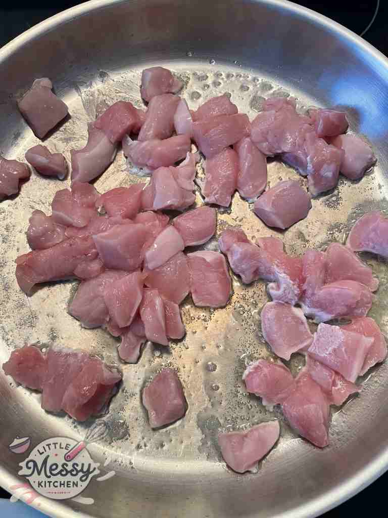 Chicken pieces cooking in a frying pan.