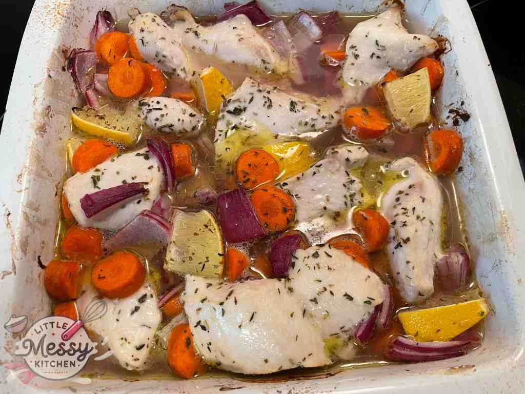 Chicken breast, chopped carrots, red onion wedges, lemon and spices mixed in a baking dish out of the oven.