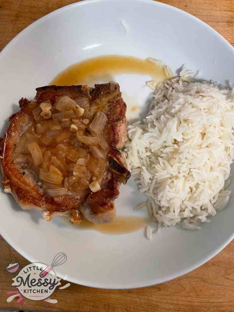 Tender pork chop served with a side of rice in a white bowl.