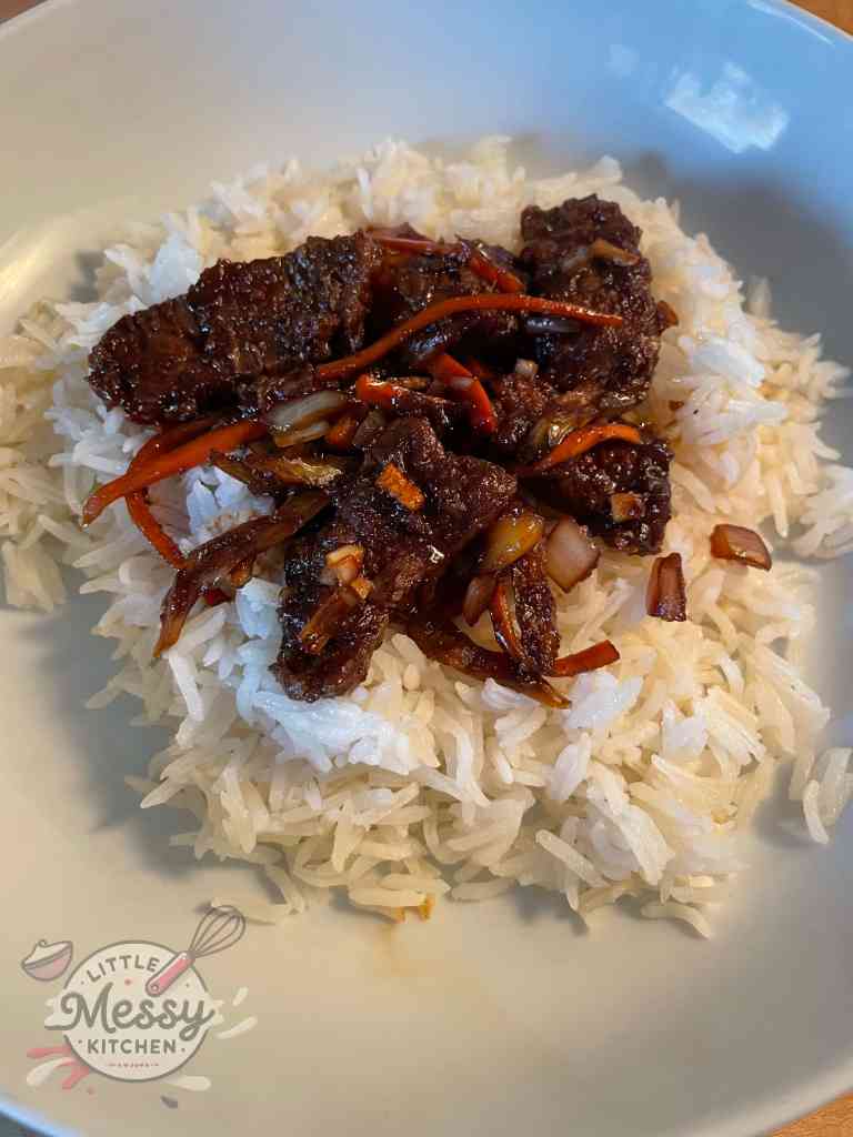 Serving of ginger beef on a bed of rice in a white bowl.